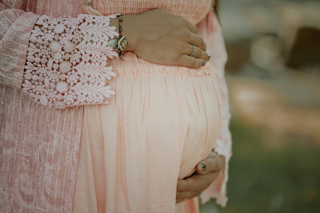 Close-up of a pregnant woman embracing her belly in a delicate pink dress.