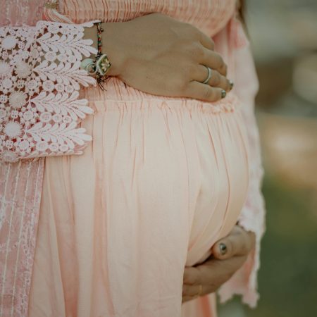 Close-up of a pregnant woman embracing her belly in a delicate pink dress.