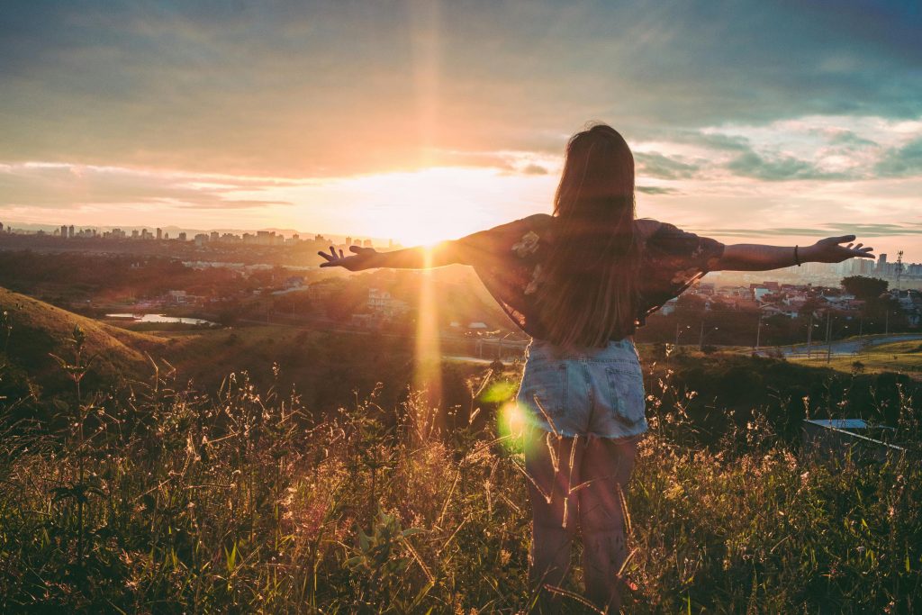 pexels-photo-847483-847483 Woman with open arms enjoying sunset view over cityscape from a grassy hilltop.